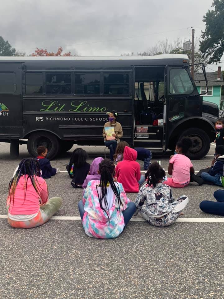 Ashley reads to a group of kids seated outside the Lit Limo bus