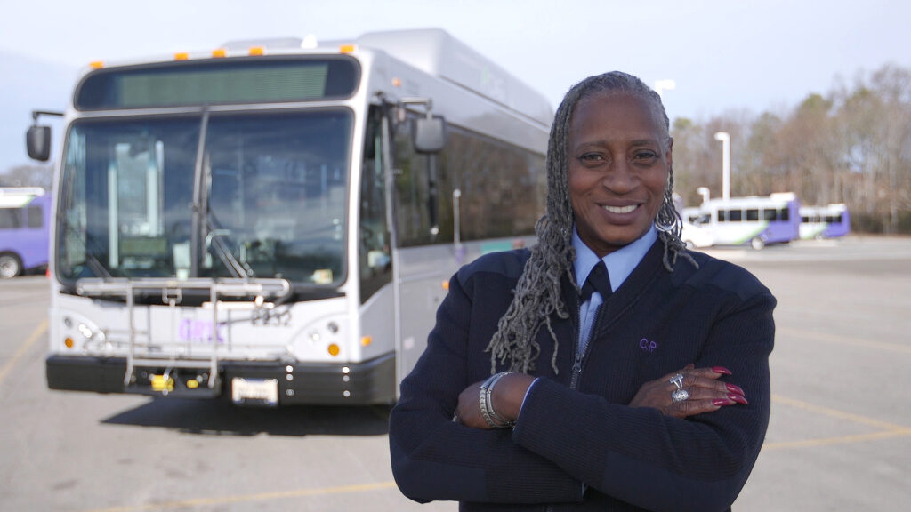 Bus operator Carol standing proudly in front of her vehicle